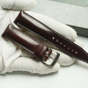 Könnte beinhalten: Zwei braune Lederarmbänder mit grüner Naht. Ein Armband hat eine silberne Schnalle.