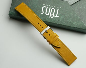 May include: A yellow leather watch strap with white stitching and a silver buckle. The strap is on a green box with the text "Tuns Leather Strap".