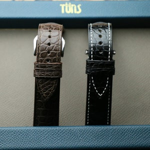 Peut inclure: Deux bracelets de montre, l'un brun et l'autre noir, sont pr&eacute;sent&eacute;s sur un fond bleu. Les bracelets sont en cuir et pr&eacute;sentent un design cousu.