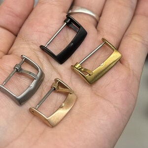 K&ouml;nnte beinhalten: Vier Uhrenarmband-Schlie&szlig;en in verschiedenen Ausf&uuml;hrungen: Silber, Schwarz, Gold und Ros&eacute;gold. Die Schlie&szlig;en sind alle gleich gro&szlig; und haben die gleiche Form, mit einem einfachen, rechteckigen Design.