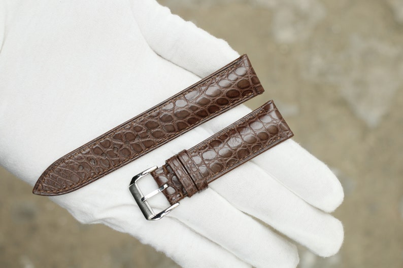 Peut inclure: Deux bracelets de montre en cuir marron avec un motif crocodile. Le bracelet de gauche est plus long et a une extr&eacute;mit&eacute; pointue. Le bracelet de droite est plus court et a une boucle.