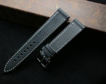 May include: Two black leather watch straps with white stitching. The straps are laid out on a black surface.