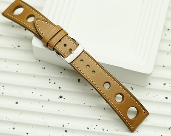 May include: A tan leather watch strap with a silver buckle and multiple holes. The strap has a stitched edge and is on a white surface.