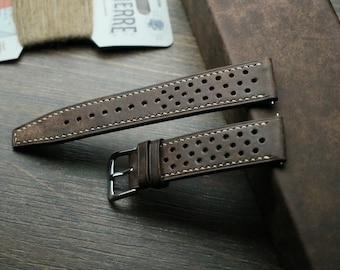 May include: Two brown leather watch straps with white stitching and a perforated design. The straps are laid out on a wooden surface.
