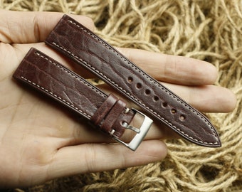 May include: Two brown leather watch straps with white stitching. The straps have a textured surface and are shown on a hand.