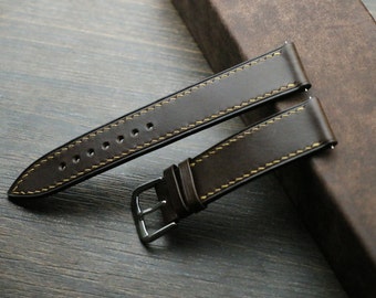May include: Two brown leather watch straps with yellow stitching. The straps are laid out on a brown surface.