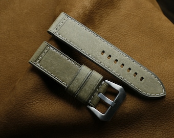 May include: Two green leather watch straps with white stitching. The straps are laid out on a brown leather surface.