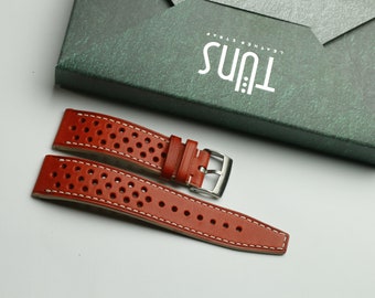 May include: A brown leather watch strap with white stitching and a perforated pattern. The strap has a silver buckle and the text "Tuns Leather Strap" is printed on a green box.