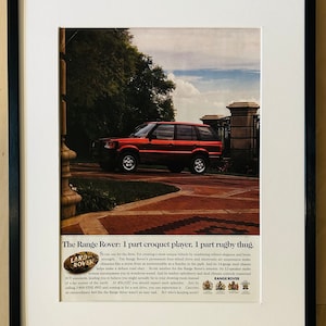 Könnte beinhalten: Ein roter Range Rover fährt auf einer gepflasterten Straße mit einem geschlossenen Eingang im Hintergrund. Der Werbetext lautet "The Range Rover: 1 part croquet player, 1 part rugby thug." und enthält das Land Rover Logo.