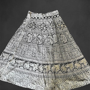 May include: A black and white wrap skirt with an intricate paisley and elephant print. The skirt has a long, flowing silhouette and is perfect for a bohemian or ethnic look.