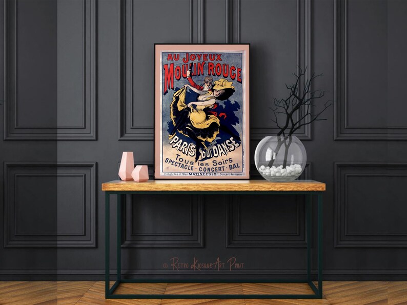 May include: A vintage poster advertising the Moulin Rouge in Paris, France. The poster features a couple dancing, with the woman wearing a yellow dress and the man wearing a red shirt. The poster is framed and hanging on a wall.
