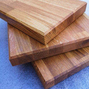 May include: Three wooden cutting boards stacked on top of each other. The boards are made of light brown wood with a natural grain pattern. The boards are all the same size and shape, and they have a smooth, polished finish.