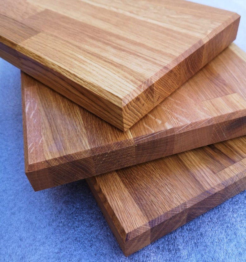 May include: Three wooden cutting boards stacked on top of each other. The boards are made of light brown wood with a natural grain pattern. The boards are all the same size and shape, and they have a smooth, polished finish.