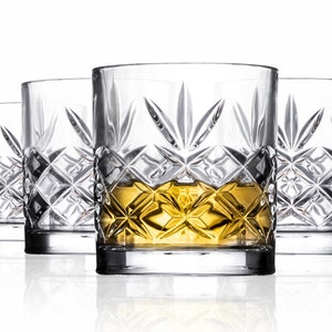 May include: Set of four clear glass whiskey tumblers with a cut glass design. The tumblers are filled with a golden liquid.
