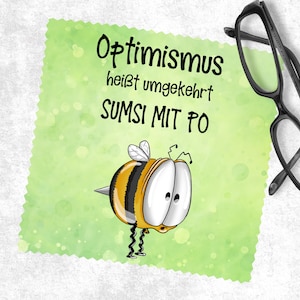 Könnte beinhalten: Eine grüne und gelbe Biene mit großen Augen und einem Stachel. Die Biene befindet sich auf einem grünen Hintergrund mit weißen Punkten. Der Text "Optimismus heisst umgekehrt SUMSI MIT PO" ist in Schwarz auf dem Hintergrund geschrieben.