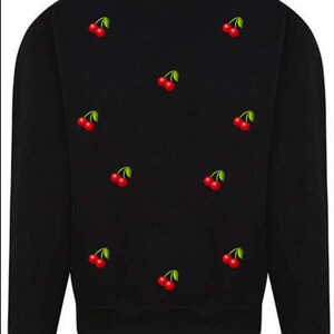 Könnte beinhalten: Schwarzer Pullover mit einem sich wiederholenden Muster aus roten Kirschen mit grünen Stielen.