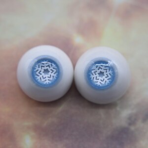 May include: Two white doll eyes with blue irises and a white snowflake design.