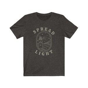 Op de afbeelding: Donkergrijs t-shirt met een vuurtoren afbeelding en de tekst "SPREAD LIGHT".