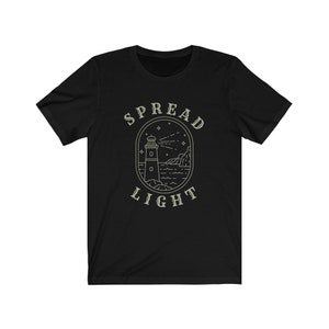 Op de afbeelding: Zwart T-shirt met een witte omtrek van een vuurtoren en de tekst "SPREAD LIGHT" in een cirkel eromheen.