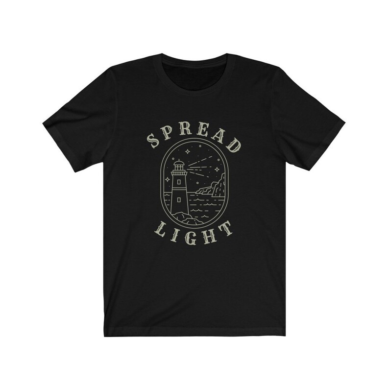 Op de afbeelding: Zwart T-shirt met een witte omtrek van een vuurtoren en de tekst "SPREAD LIGHT" in een cirkel eromheen.