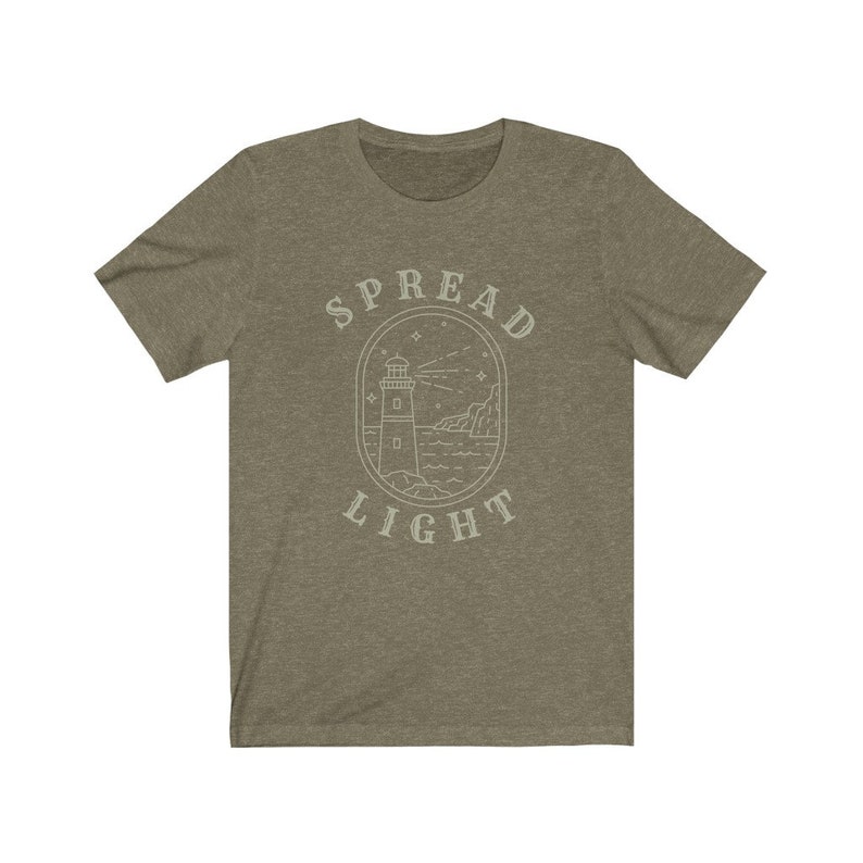 Op de afbeelding: Een groen T-shirt met een witte omtrek van een vuurtoren en de tekst "SPREAD LIGHT" in een cirkel eromheen.