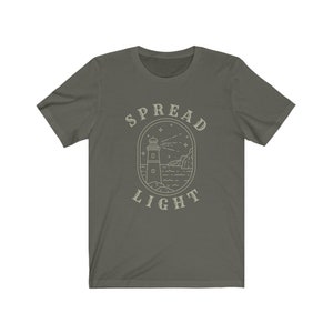 Op de afbeelding: Een donkergroen T-shirt met een witte omtrek van een vuurtoren en de tekst "SPREAD LIGHT" in een cirkel eromheen.