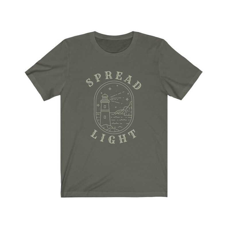 Op de afbeelding: Een donkergroen T-shirt met een witte omtrek van een vuurtoren en de tekst "SPREAD LIGHT" in een cirkel eromheen.