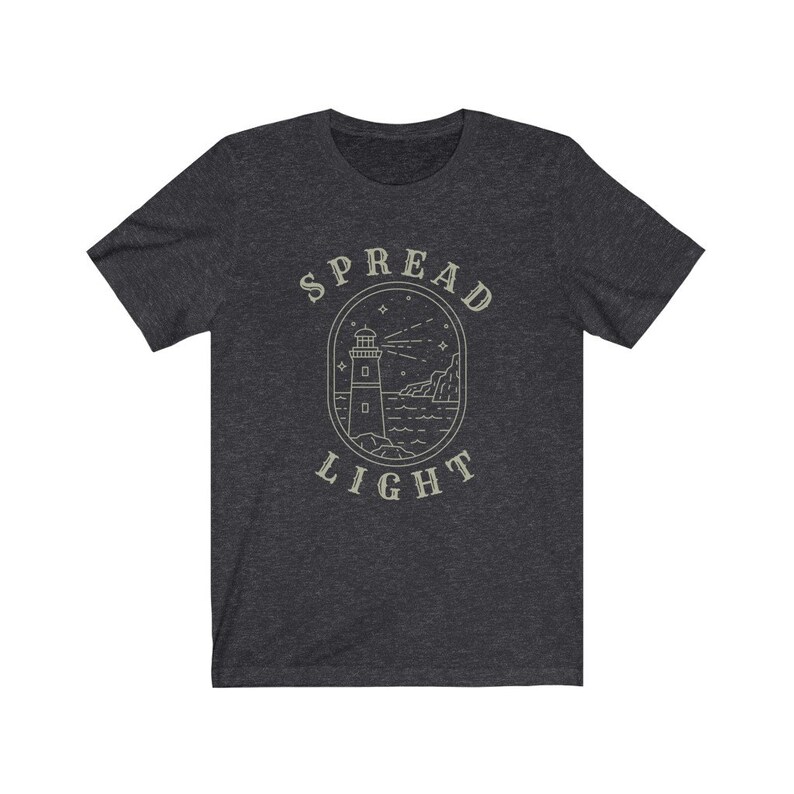 Op de afbeelding: Donkergrijs t-shirt met een vuurtoren afbeelding en de tekst "SPREAD LIGHT" in een witte omtrek.