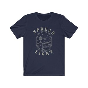Op de afbeelding: Donkerblauw T-shirt met een vuurtorenafbeelding en de tekst "SPREAD LIGHT" in een vintage-ge&iuml;nspireerd lettertype.