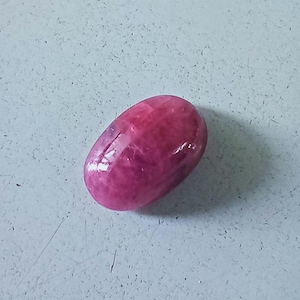 May include: A smooth, oval-shaped, pink gemstone with a slight sheen.