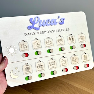 May include: A rectangular wooden daily responsibilities chart with the name Luca's in purple script. It features two rows of icons with sliding toggles showing red or green. Icons include bed, clothes, food, hair, shoes, lunchbox, bike, book, TV, and toothbrush.