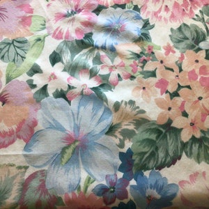 May include: A white fabric with a floral pattern featuring pink, blue, and green flowers. The fabric has a soft, textured feel.