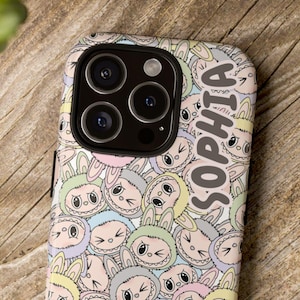 May include: A phone case with a repeating pattern of cartoon bunny faces in pastel colors. The name "SOPHIA" is printed vertically on the side of the case. The case is on a wooden surface.