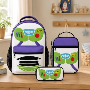Op de afbeelding: Een set witte, paarse en groene rugzak, lunchtas en etui. Het ontwerp lijkt op het gezicht van een stripfiguur, met de naam "OLIVER" op elk item. De rugzak heeft zwarte mesh zijzakken.
