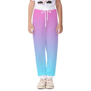 May include: Gradient pink, purple, and blue sweatpants with a white drawstring. The waistband features a white background with colourful sprinkles. The trousers are worn with a white t-shirt and white trainers.