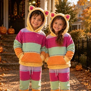 May include: Two matching hooded loungewear sets featuring horizontal stripes in magenta, mint green, and orange. Each set includes a long-sleeved hoodie with cat ears on the hood and a front kangaroo pocket, paired with matching elastic-waist pants.