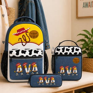 May include: A backpack, lunch bag, and pencil case set featuring a yellow top, white and black cow print accents, and blue denim-style fabric. The items are personalized with the name AVA in a western-themed font with cowboy hats and boots.