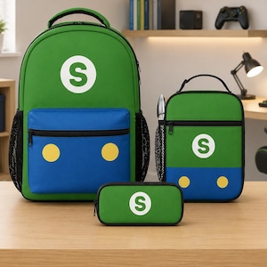 May include: A green and blue backpack, lunch bag, and pencil case set. Each item features a white letter S inside a white circle, a blue front panel, and two yellow circles. The backpack includes black mesh side pockets and a top handle.