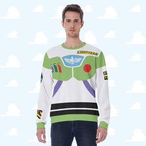 Puede incluir: Sudadera blanca de manga larga con un diseño de disfraz de Buzz Lightyear. La camisa tiene detalles en verde y morado, con la palabra "LIGHTYEAR" impresa en el hombro. El diseño incluye un emblema en el pecho y otros detalles.