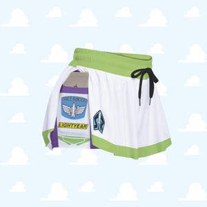 Puede incluir: Falda blanca con ribete verde y cordón negro. La falda presenta un diseño inspirado en el personaje Buzz Lightyear, con las palabras "SPACE RANGERS" y "LIGHTYEAR" visibles en la parte delantera.