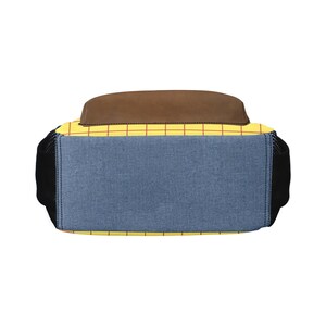 May include: A backpack featuring a yellow base with a red grid pattern, a solid brown top panel, and a blue denim-textured front pocket. The sides are black mesh, and the design incorporates a structured rectangular shape with visible stitching.