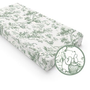 Può includere: Una fodera per fasciatoio bianca e verde con un motivo toile raffigurante i personaggi di Winnie the Pooh e scene di foresta. La fodera ha un angolo arrotondato e una grafica circolare di Winnie the Pooh con un barattolo di miele.