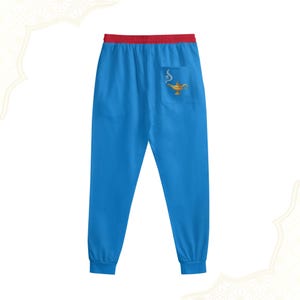 Pode incluir: Calças de moletom azuis com cós vermelho e bolso com design de lâmpada dourada. As calças têm um corte folgado com punhos elásticos, perfeitas para uso casual.