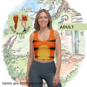 Puede incluir: Un top corto naranja con rayas negras y un diseño de círculo amarillo. Las palabras "También disponible" son visibles, junto con "Los artículos se venden por separado". La modelo lleva leggings grises. El fondo presenta una ilustración de dibujos animados.