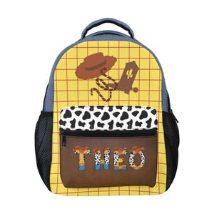 May include: A backpack featuring a yellow grid pattern with a brown cowboy hat and boot graphic. The front pocket has a black and white cow print section above a brown panel displaying the name THEO in letters styled like a cowboy outfit.