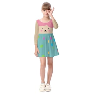 May include: A girl wearing a blue and pink dress with a cartoon animal face on the front. The dress has colorful polka dots. She is wearing white sneakers.