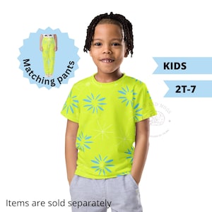 May include: A child in a neon green t-shirt featuring a blue floral and starburst design, paired with grey shorts. The image includes text that reads "KIDS 2T-7" and "Matching pants".
