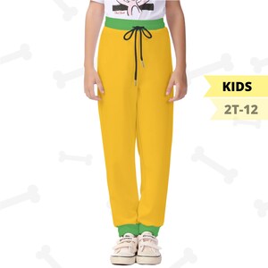 May include: Yellow children's sweatpants with a green waistband and cuffs. The trousers have a black drawstring and are worn with white trainers. The image includes the text "KIDS 2T-12".