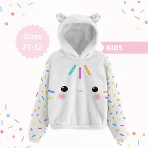 May include: White hooded sweatshirt with a cartoon face design, featuring black eyes, pink cheeks, and colorful sprinkles on the sleeves. The hoodie has small ear-shaped details on the hood. Sizes 2T-12.
