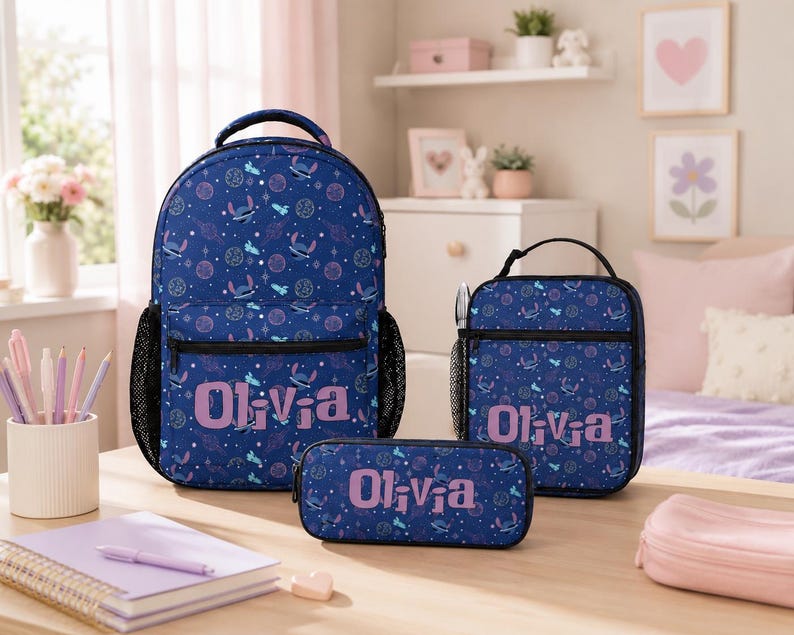 Op de afbeelding: Een set bestaande uit een donkerblauwe rugzak, lunchtas en etui met een herhalend patroon van Stitch, planeten en sterren. Elk item is gepersonaliseerd met de naam Olivia in lichtpaarse letters en is voorzien van zwarte ritsen en zijvakken.